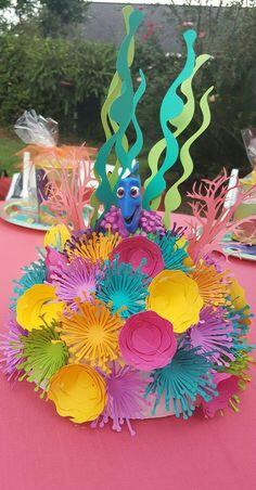 Пін може містити: a colorful centerpiece with paper flowers and sea creatures on it's head is sitting on a pink table cloth