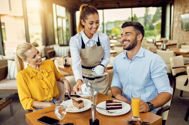 Happy waitress serving coffee to a couple who is eating cake in a cafe